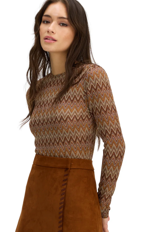 A woman wearing a long-sleeve knit top with a brown, beige, and rust zigzag pattern, paired with a brown skirt, against a plain white background.